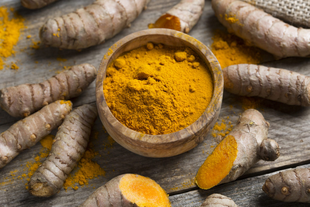 Turmeric powder in a bowl surrounded by freshly cut rhizomes