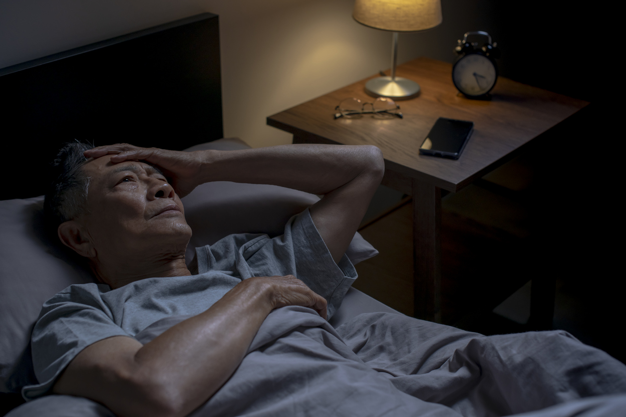 Depressed senior Asian man lying in bed cannot sleep from insomnia